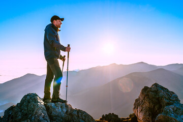 Wall Mural - hiker man standing with trekking poles on a cliff edge and looking at tatra mountains valley covered