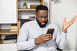 Confused puzzled African-American man in smart casual shirt holding smartphone and expressing misunderstanding, spreads his hands in incomprehension
