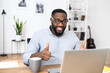 © Vadim Pastuh - Happy and excited African-American employee in glasses sitting at the desk, working from home, raising thumbs up to his colleagues while on a meeting call, using the laptop to video chat with the team