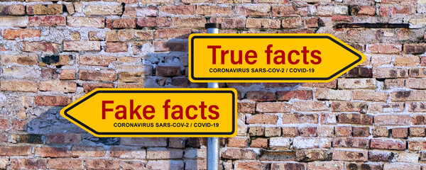 Wall Mural - two street signs with message TRUE FACTS and FAKE FACTS regarding the coronavirus SARS-COV-2, COVID-19 in front of a brick wall
