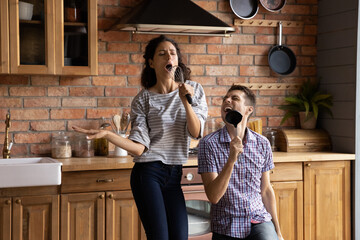 Wall Mural - Overjoyed millennial Caucasian man and woman have fun dancing singing in modern kitchen at home. Excited happy young couple feel playful enjoy good morning in new own house or flat. Rental concept.