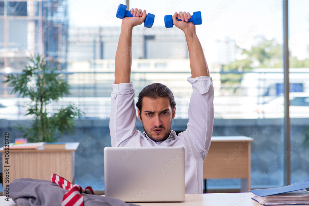 Young male employee doing sport exercises in the office - obrazy, fototapety, plakaty 