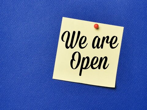 Text we are open written on yellow paper note with pin board over blue background.Business concept.