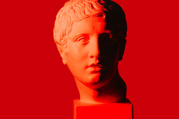 Wall Mural - Red-lit half-shaded marble head of young man over red background. On a square pedestal. Shadow covering half of the face. Frontal view.