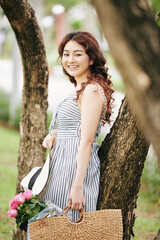 Wall Mural - Portrait of lovely young Vietnamese woman with basket of light pink roses standing in city park