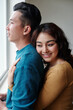 © DragonImages - Happy pretty young woman hugging her husband from behind when they are standing near window