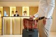 © DragonImages - Cropped image of hotel guest standing in lobby with luggage after checking in