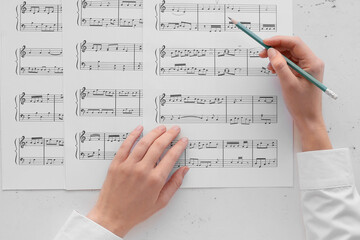 Wall Mural - Female hands with pencil and music sheets on light background