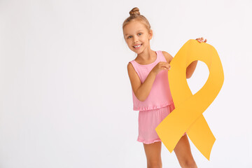 Little girl with golden ribbon on light background. Childhood cancer awareness concept