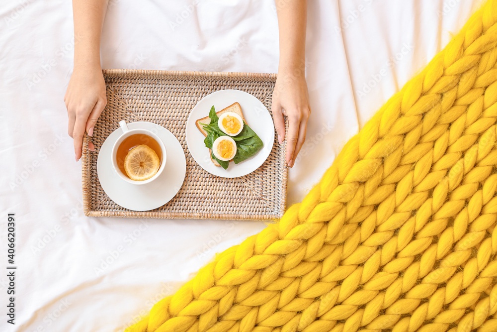 Woman holding tray with tasty breakfast on bed, top view