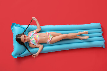 Wall Mural - Cute little girl lying on inflatable mattress against color background