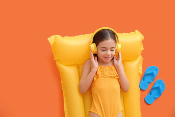 Wall Mural - Cute little girl with headphones lying on inflatable mattress against color background