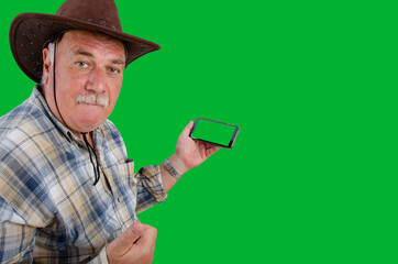 An old rancher liked something. He looks at the camera with a serious face. The man shows his thumb with right hand. The left one holds a smartphone with a green screen. Taken on a green background.