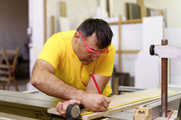 Carpenter taking measurement of a wooden plank with pencil and ruler