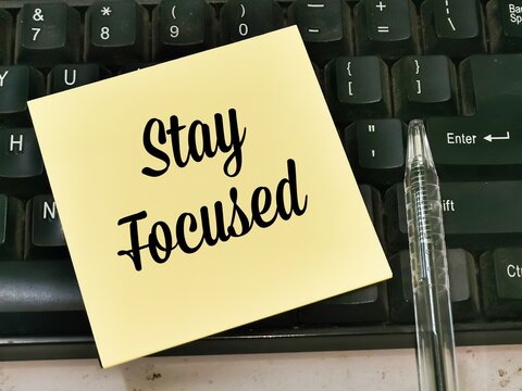 Text STAY FOCUSED written on brown paper note on computer keyboard with a pen.Motivational quote.