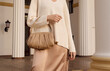 canvas print picture - Closeup beige leather bag in hand of fashion woman in silk skirt. Elegant fall and spring outfit.