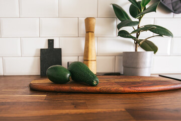 Kitchen brass utensils, chef accessories. Hanging kitchen with white tiles wall and wood tabletop.Green plant and avocado on kitchen background