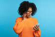 © DimaBerlin - Studio portrait of confused shocked African ethnicity woman looking at smartphone with opened mouth, reading bad news, notification, unpleasant message isolated on blue color background.