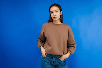 Wall Mural - Young woman in hoodie posing in studio on blue background