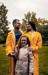 Family of three in raincoat enjoying together in city park.