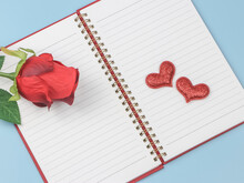 Two Red Glitter Hearts And Red Rose On Opened Notebook On Blue Background.. Valentine's Day