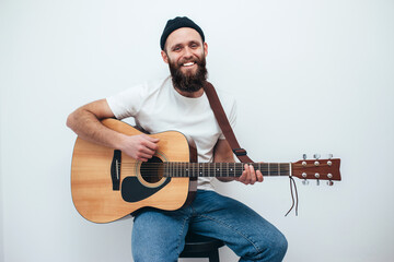 A young stylish guy with a beard plays the guitar isolated on a white background