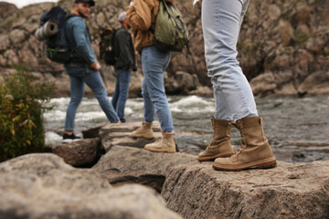 Wall Mural - Group of friends with backpacks crossing mountain river, focus on hiking boots