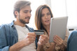 © opolja - Laughing couple sitting on the couch shopping online with tablet pc at home in the living room.