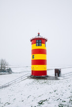 Lighthouse In The Snow. Small Lighthouse In Red And Yellow. Lighthouse On A Dike On The North Sea. Light Tower With Snow In Winter