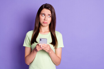 Photo portrait of sad upset girl texting message on smartphone crying looking at blank space isolated on bright purple color background