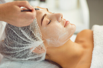 Wall Mural - Hands of beautician applying moisturizing mask or cream to young smiling womans face