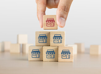 Franchise growth, business growth or distribution management concept. Wooden blocks with the shop icon arranged in pyramid stair shape and a man is holding the top one.