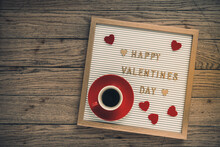White Board With Gold Lettering For Valentines Day, Red Hearts And A Red Cup Of Espresso Coffee On Rustic Wooden Background, Top View