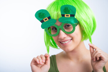 Cheerful young woman in green wig and funny glasses celebrating st patrick's day on a white background. Copy space