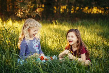 Happy children girls playing dolls in park. Cute adorable kids sitting in grass on meadow playing toys. Happy childhood authentic lifestyle. Summer backyard activity for kids outdoors.