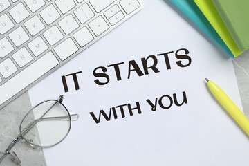 Poster - Sheet of paper with phrase It Starts With You, keyboard and stationery on grey table, flat lay