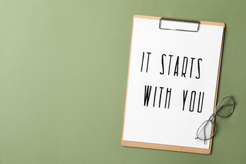 Poster - Clipboard with phrase It Starts With You and glasses on green background, flat lay. Space for text