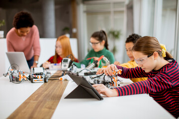 Wall Mural - Happy kids with their African American female science teacher with laptop programming electric toys and robots at robotics classroom