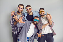 Happy Best Friends Having Fun While Hanging Out Together. Group Of 4 Young Men In Sunglasses Smiling, Looking At Camera And Posing For Funny Photo In Studio With Light Gray Background