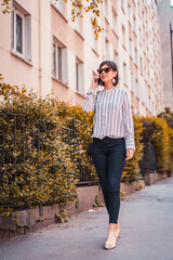 Wall Mural - Young urban business woman talking on phone on city street 