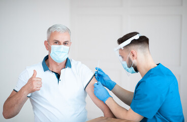 Poster - Mature man showing thumb up, receiving covid-19 vaccine injection during his visit to doctor at health centre