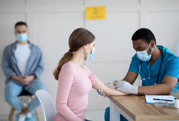 Poster - African American doctor injecting covid-19 vaccine to young woman at clinic. Immunization against global virus