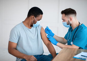 Poster - Medical doctor or nurse giving coronavirus vaccine shot to African American male patient at clinic