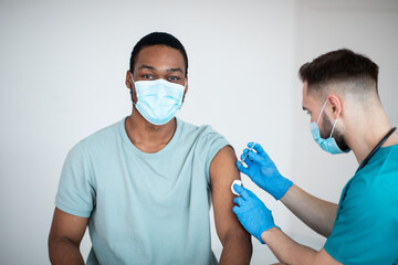 Poster - Immunization and health care system. Black male patient visiting doctor, receiving covid-19 vaccine injection at clinic