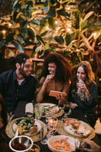 Diverse Group Of Friends Laughing And Having Fun With Phone At Garden Dinner Party