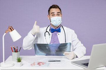 Wall Mural - Male happy doctor man wearing medical gown sterile face mask latex gloves hold X-ray of lungs fluorography roentgen show thumb up gesture isolated on violet background Healthcare medicine concept