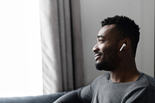 Close-up side view on handsome African-American guy with an airpods earphones spends time at home, listening music