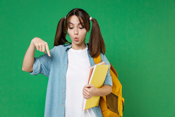 Wall Mural - Shocked young woman student in blue shirt backpack hold notebooks pointing index finger down isolated on green color background studio portrait. Education in high school university college concept.