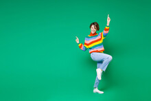 Full Length Side View Of Cheerful Funny Young Brunette Woman 20s In Casual Colorful Sweater Dancing Pointing Index Fingers Up Winner Gesture Isolated On Bright Green Color Background Studio Portrait.