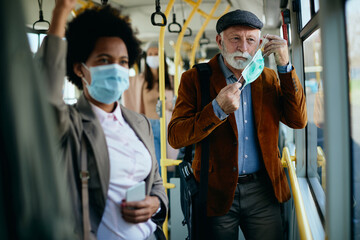 Wall Mural - Mature man putting on protective face mask in a public transport.